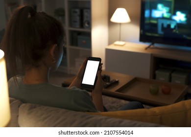 Teenager relaxing on the couch at home and connecting online using her smartphone, screen mock-up - Shutterstock ID 2107554014