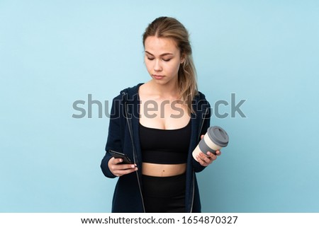 Teenager Russian girl holding mat isolated on blue background holding coffee to take away and a mobile