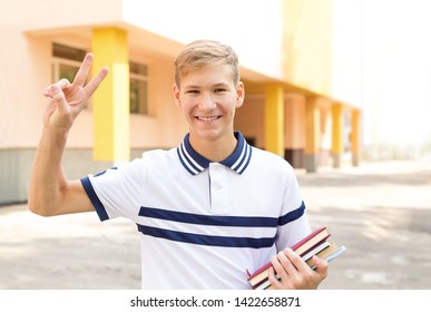 Teenager school student shows a gesture V of success against the background of the school. To study in college abroad.