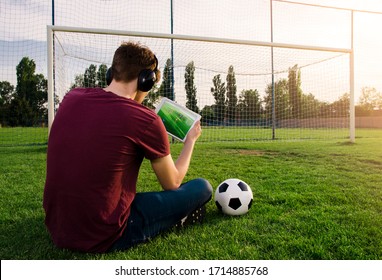 Teenager sitting alone on soccer field watching game/playing video game of football on tablet - Powered by Shutterstock