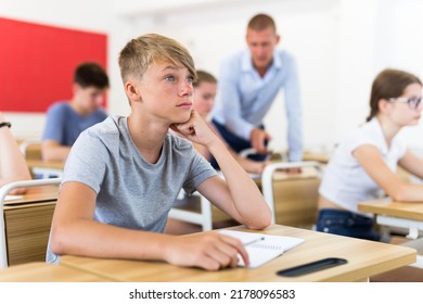 Teenager Sitting In Class Room. Male Teacher Explaining Something To Them.