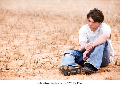 Teenager Sitting Depressed In Dry Lake Bed Amongst The Weeds, Contemplating.