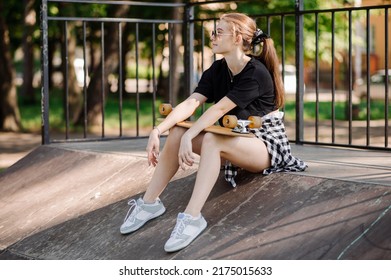 Teenager Skater Girl Is Sitting And Resting On The Ramp In The Skate Park