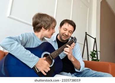 Teenager son learning to playing an acoustic guitar with father support. Happy single parent family relations, loving father teaching son - Powered by Shutterstock