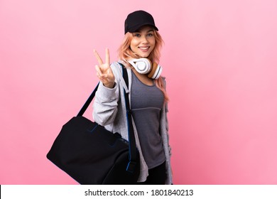 Teenager sport woman with sport bag over isolated background smiling and showing victory sign