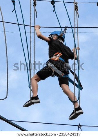 A teenager in sports equipment is crossing a suspended suspension rope bridge against the background of a blue sky. View from below