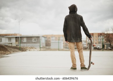 Teenager Standing In A Black Hoodie Holding A Hand Skateboard On The Background Urban Slum