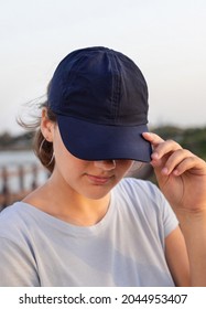 Teenager Standing By The Sea At Sunset. Teen Girl Wearing T-shirt And Dark Blue Baseball Cap And Touching The Visor. Cap And T-shirt Mockup