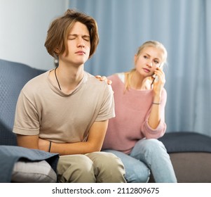 Teenager with stomach ache sitting on couch at home and holding his stomach with hands while worried mom calling doctor on phone - Shutterstock ID 2112809675
