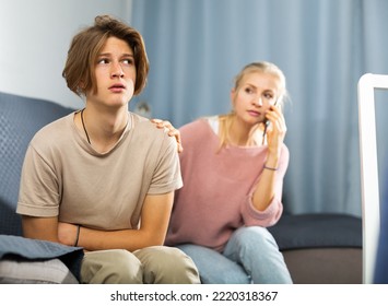 Teenager with stomach ache sitting on couch at home and holding his stomach with hands while worried mom calling doctor on phone - Shutterstock ID 2220318367