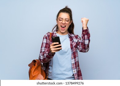 Teenager Student Girl Over Isolated Blue Wall With Phone In Victory Position