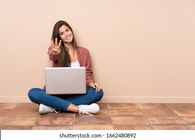 Teenager Student Girl Sitting On The Floor With A Laptop Happy And Counting Four With Fingers