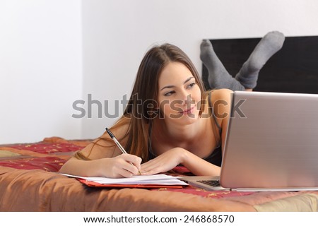 Teenager student studying with a laptop and taking notes lying in her bedroom