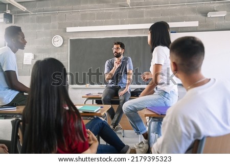 Teenager students listening and talking to friendly young male teacher - Group discussion in High School Education