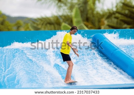 Teenager surfing in beach wave simulator attraction in water amusement park of tropical resort. Teen age boy trying to ride body board. Surf fun. Young surfer during training on generated waves