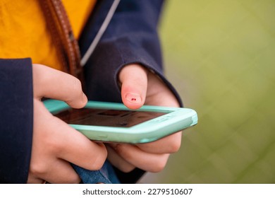 A teenager types on a cellphone. The teenager has chipped nail polish, and the cellphone is in a green case. 