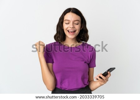 Teenager Ukrainian girl isolated on white background using mobile phone and doing victory gesture