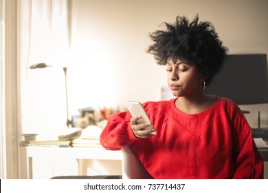 Teenager Using Her Smart Phone Sitting At Home In Her Bedroom