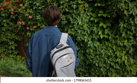 A Teenager, Wearing A Denim Jacket And A Rucksack With Communist Pins Among The Vine In Summer.