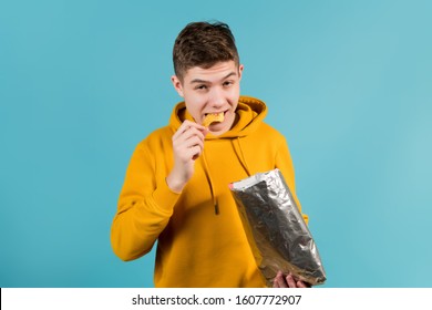 teenager in a yellow sweatshirt on a blue background eats chips - Powered by Shutterstock