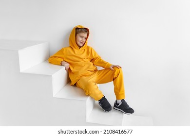 a teenager in a yellow tracksuit on a monochrome background in a hood is sitting on the steps