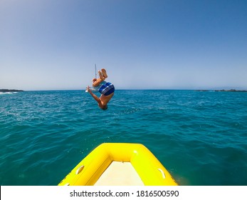 Teenager And Young Man Jump And Doing A Backflip In The Boat Or Dinghy To The Water Having Fun And Enjoying Summer Vacations In The Ocean - Caucasian People At The Beach Renting A Boat