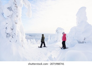 Teenagers brother and sister hiking in snowshoes in winter forest among snow covered trees in Lapland Finland