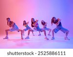 Teenagers, girls dressed casual attire dancing hip-hop in neon light against gradient pink background. Rhythm and energy. Concept of sport and hobby, childhood, friendship, motion. Dance school.