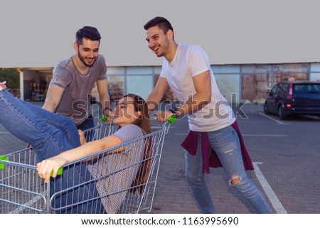Teenagers having fun near the supermarket while drive shopping cart. Young and Careless concept.