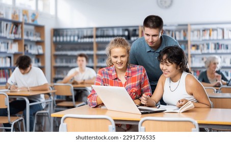 Teenagers noisily discussing something while looking at laptop screen in the school library - Powered by Shutterstock