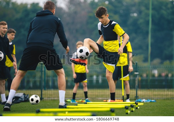 Teenagers on soccer training camp. Boys practice\
football with young coaches. Junior level athletes improving soccer\
skills on outdoor training. Player kick soccer ball to coach and\
ladder skipping