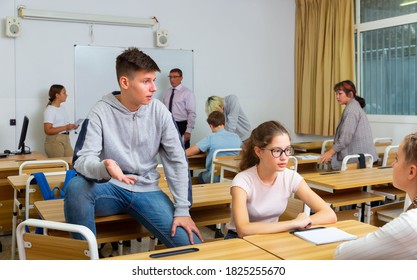 Teenagers Students Of Middle School Chatting On Break Sitting At Desks