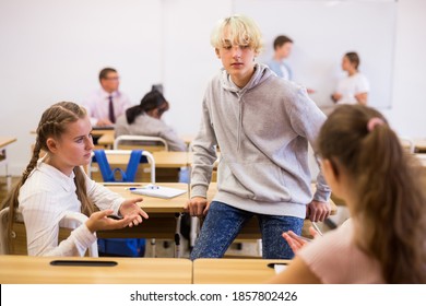 Teenagers Students Of Middle School Chatting On Break Sitting At Desks