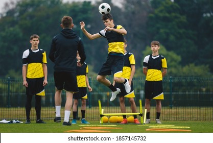 Teenagers training soccer headshot. Young player jumping high and head ball. Coach coaching junior youth football club. Team waiting in line in the background.  - Powered by Shutterstock