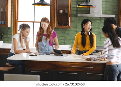 Teens collaborating on school project in kitchen, using tablet and papers. Collaboration, teamwork, brainstorming, technology, education, homework