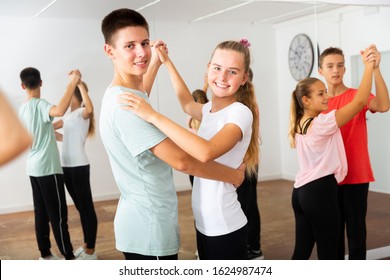 Teens in pairs learning to dance waltz with young female choreographer in modern studio 