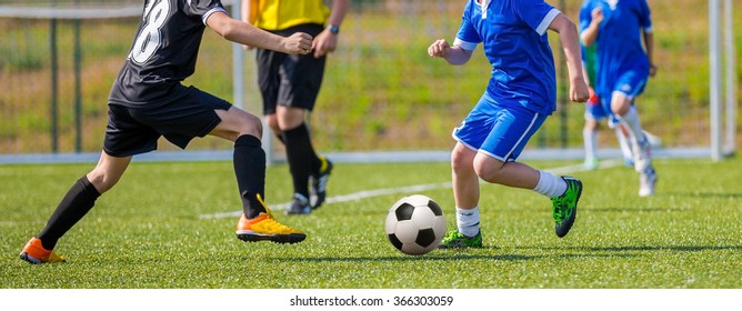 Teens Playing Soccer Football Match. Competition Between Two Youth Soccer Teams. Boys In Blue And Black Sport Uniforms Running And Kicking Soccer Ball On A Pitch. Football Soccer Tournament.