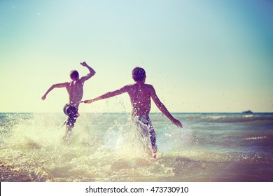 Teens Running Into The Waves At The Beach, Instagram Filter. Focus On Water Spray