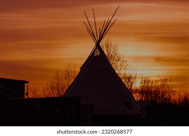 A teepee is silhouetted against the setting sun - Powered by Shutterstock