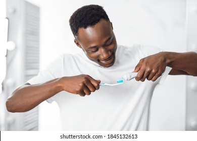 Teeth Cleaning Concept. Black Guy Applying Toothpaste On Toothbrush Brushing Teeth Standing In Modern Bathroom At Home In The Morning. Male Oral Hygiene Toothcare Routine