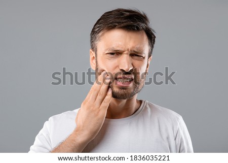 Teeth problem. Man suffering from strong tooth pain, grey studio background, copy space. Upset middle-aged man rubbing his cheek, got teeth inflammation, pulpitis or dental caries