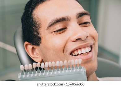 teeth shades palette near male mouth. African american man at dental clinic