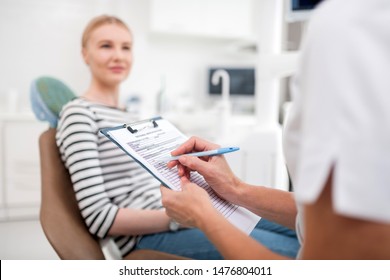 Teeth Treatment. Dentist Sitting In Her Office In Front Of Her Smiling Patient And Writing Prescriptions For Her.