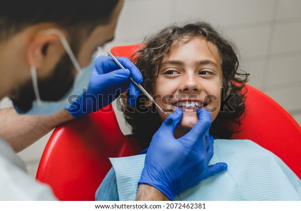 Teeth whitening. Smiling caucasian boy visiting\
dentist stomatologist orthodontist, curing tooth, putting braces in\
dental clinic.