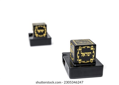 Tefilina o filacterias. Par de cajas negras de cuero para el brazo y para la cabeza con tiras de cuero que contienen versos de Torah que son oraciones de hombres judíos usados. Una caja con la letra hebrea Shin.