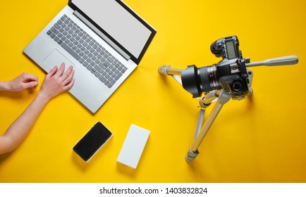 Tehnobloger Concept. Women's Hands Unboxing New Smartphone With Box And Blogging With Camera On Tripod, Laptop On Yellow Background. Top View