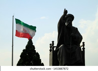 Tehran, Iran - June 10, 2018: A Large Iranian Flag Waving In The Wind Behind A Statue Of Khomeini In Tehran, Iran