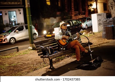 TEL AVIV, ISRAEL - October 12, 2013: Blind Street Musician And Singer With Guitar Sitting On A Bench On Rothschild Boulevard At Night