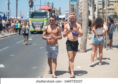 Tel Aviv - June 14th 2019: Pride Parade: Couple Of Young Men Walking Shirtless Down Herbert Samuel Road. Truck Pulling A Parade Float In Far Background.