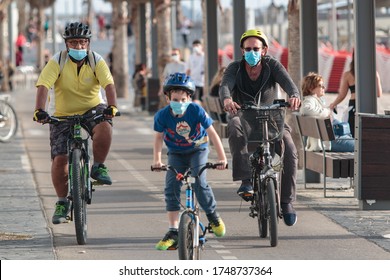 Tel Aviv – May 4th 2020: Corona epidemic lifestyle – Athletic Adult men with face masks on, riding bicycles at the beach promenade. Blurred Masked kid riding in foreground.